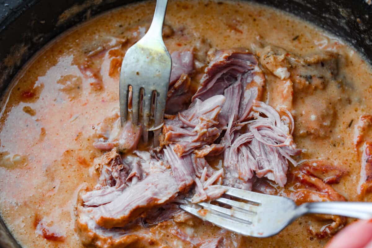Someone using two forks to shred the pork in the slow cooker. 