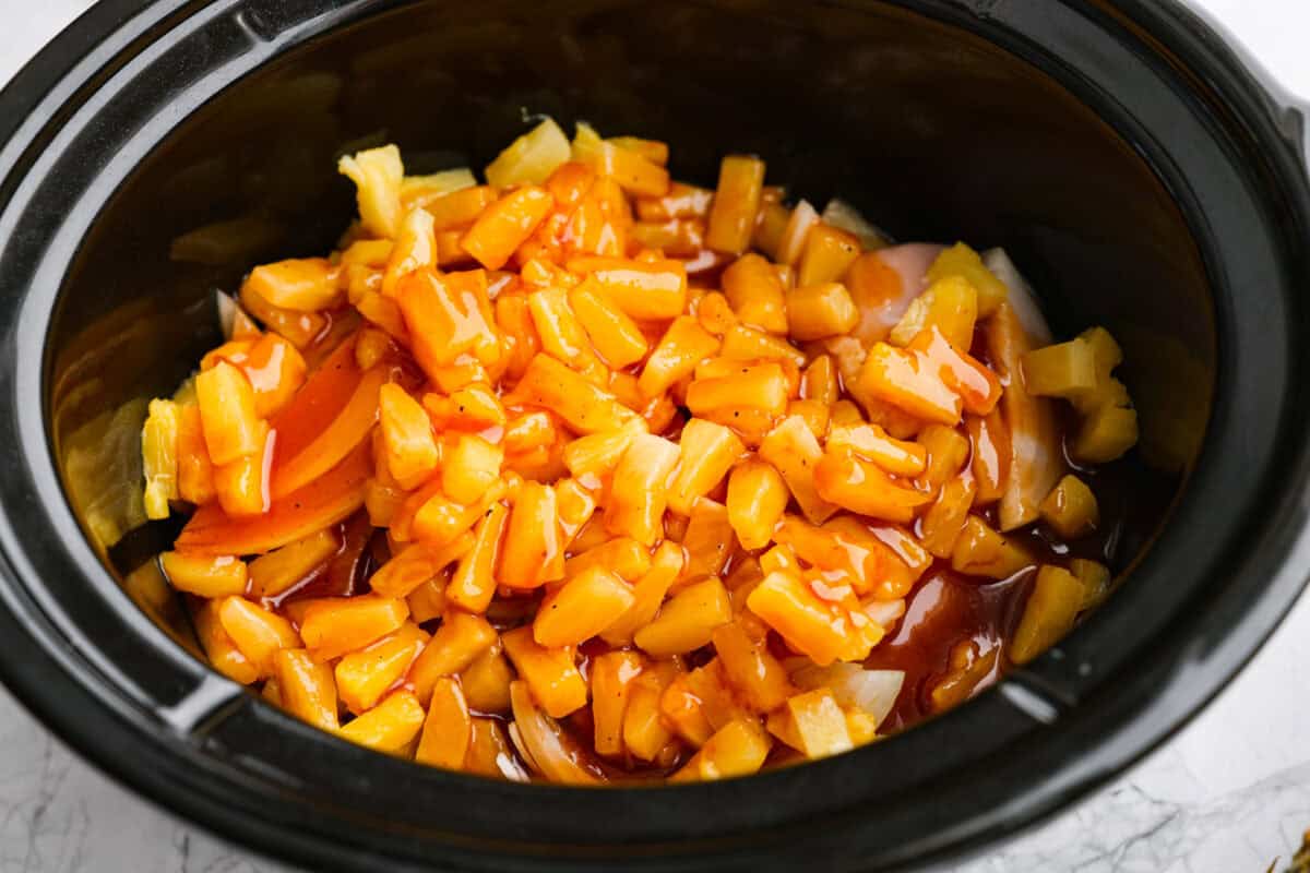 Sauce poured over the pineapple, onion, and chicken in the slow cooker. 