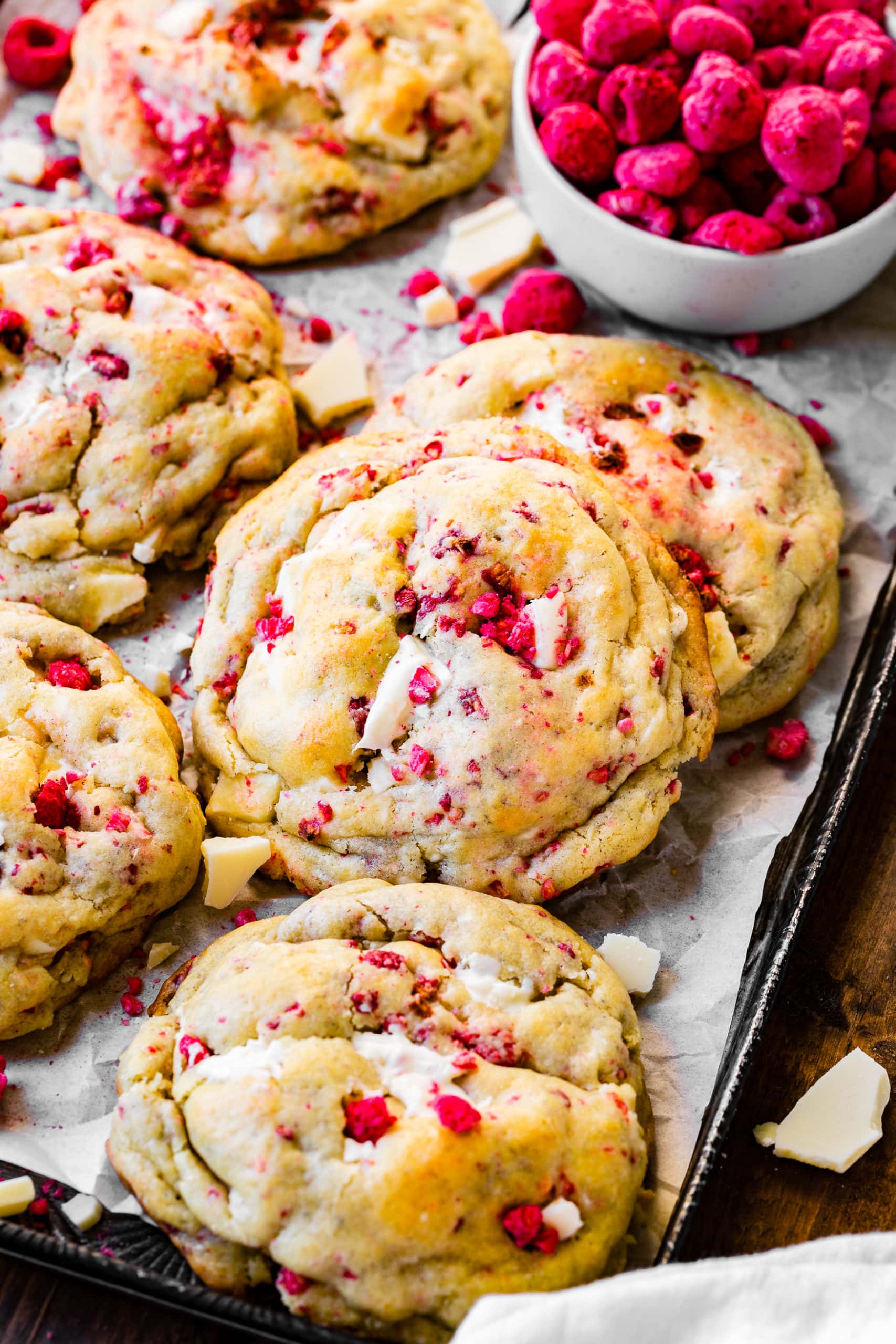 a photo of several perfectly baked thick and chewy raspberry white chocolate cookies laying on a parchment lined baking sheet.