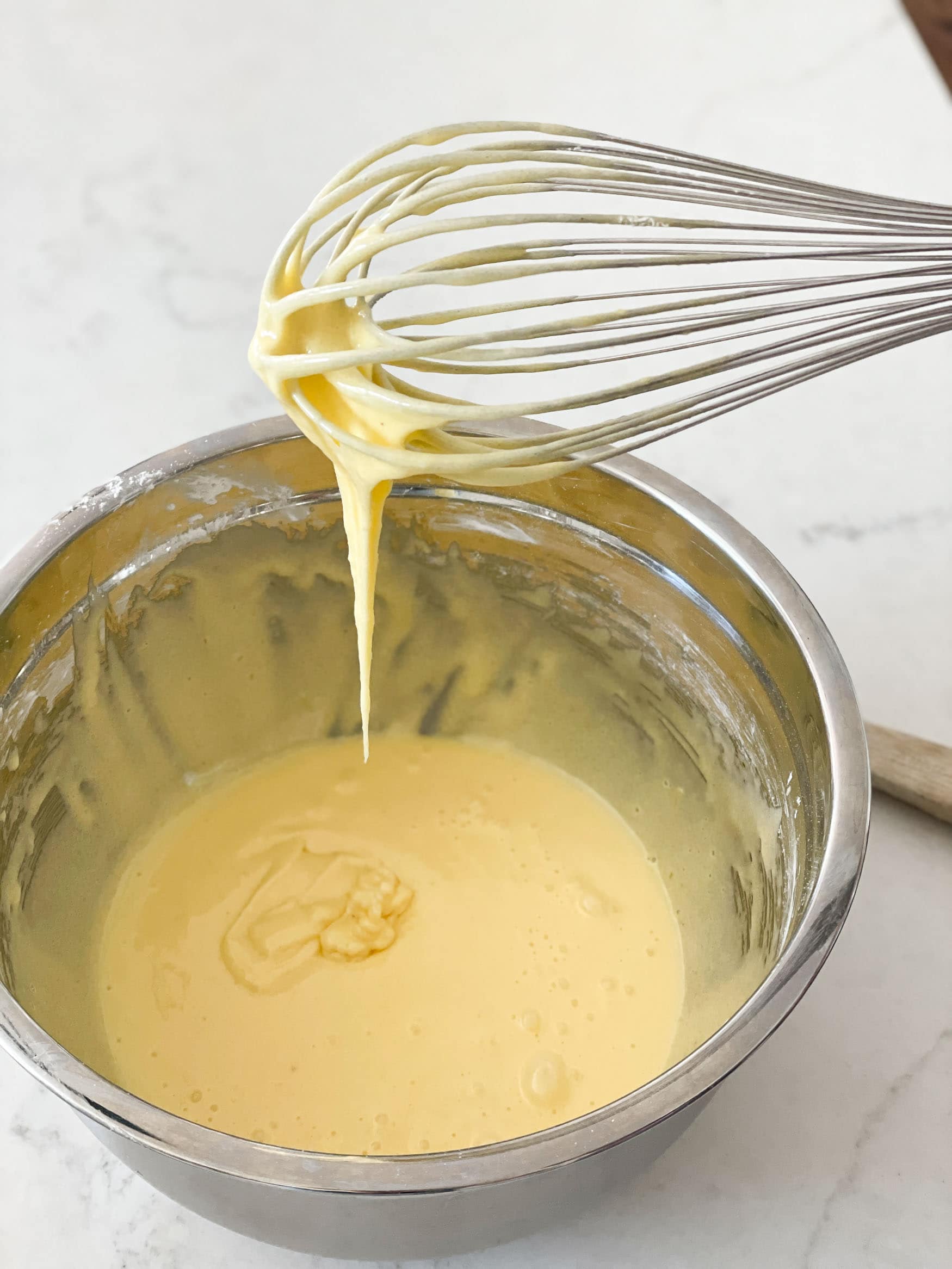 a photo of coconut instant pudding being whisked in a large metal mixing bowl.