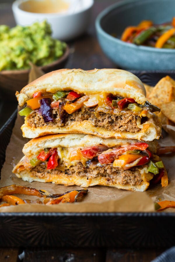 a photo of a mexican fajita burger that has been cut in half and stacked on top of each other so you can see the inside of the burger topped with onions and peppers a photo of a mexican fajita burger that has been cut in half and stacked on top of each other so you can see the inside of the burger topped with onions and peppers