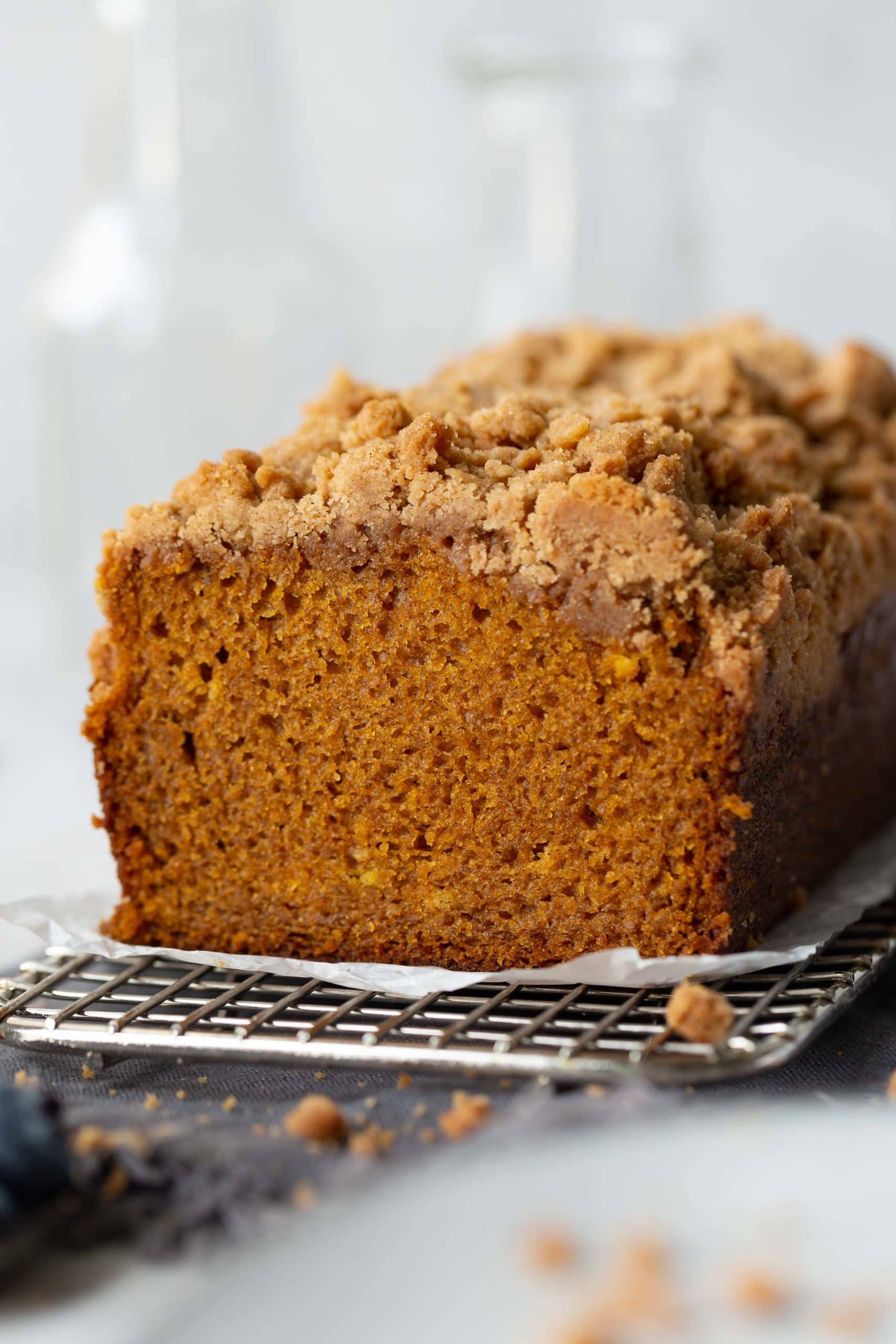 a photo of the cross section a loaf of pumpkin bread with cinnamon crumb topping sitting on a wire cooling rack.