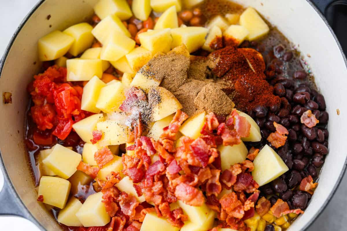 Veggies, beans, bacon, broth, and seasonings added to the cooked meat mixture.
