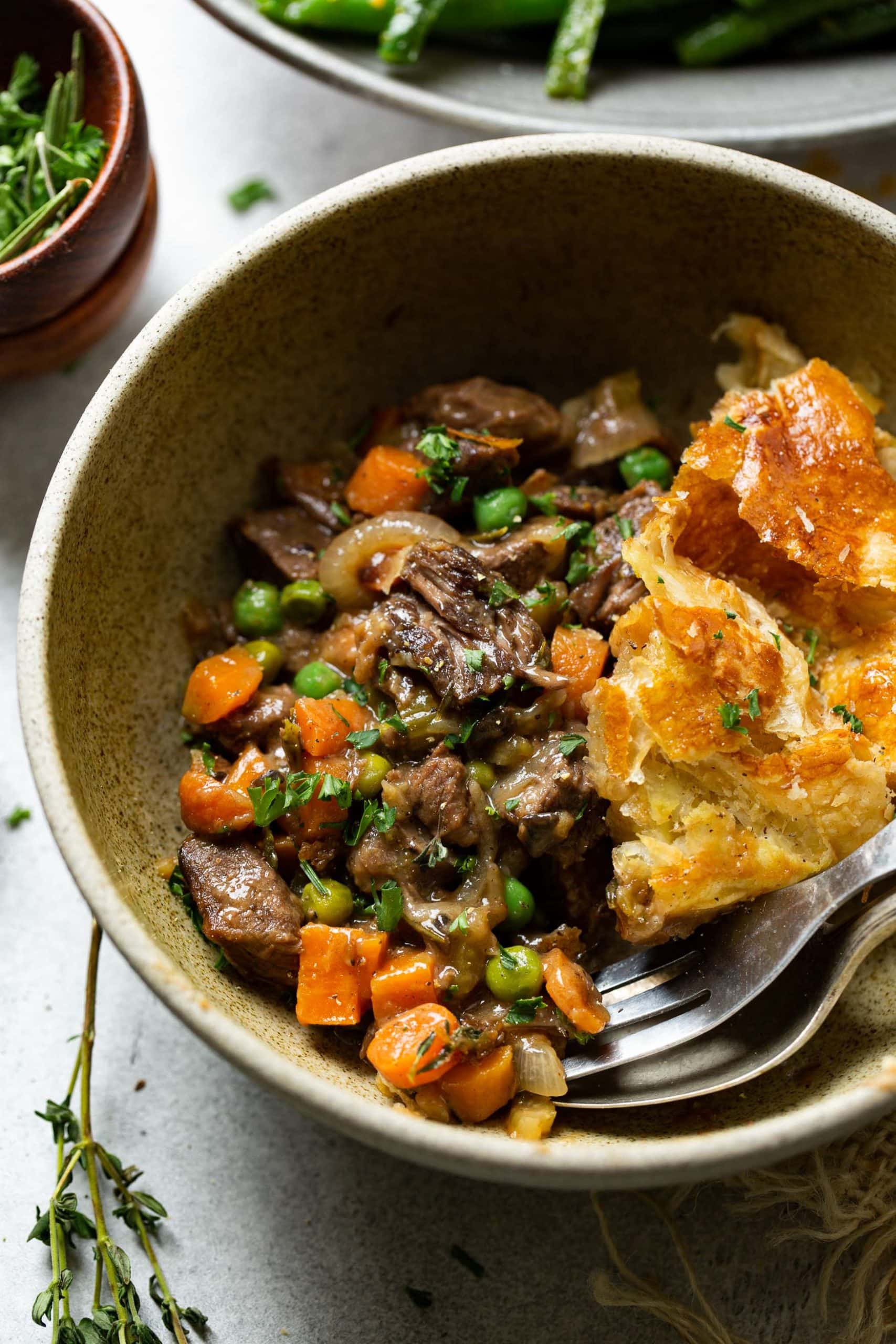a photo of a bowl full of a serving of beef pot pie that is loaded with vegetables and topped with a golden pie crust.