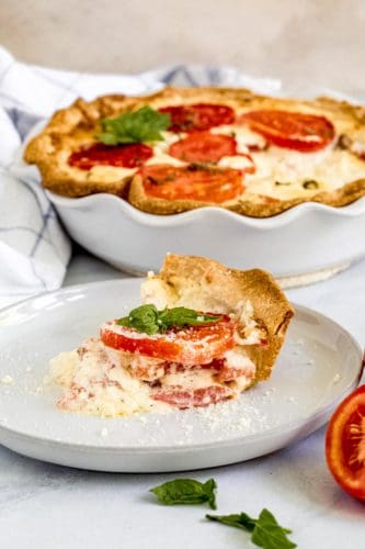 Alabama Tomato Pie slice on white plate with pie dish behind it.