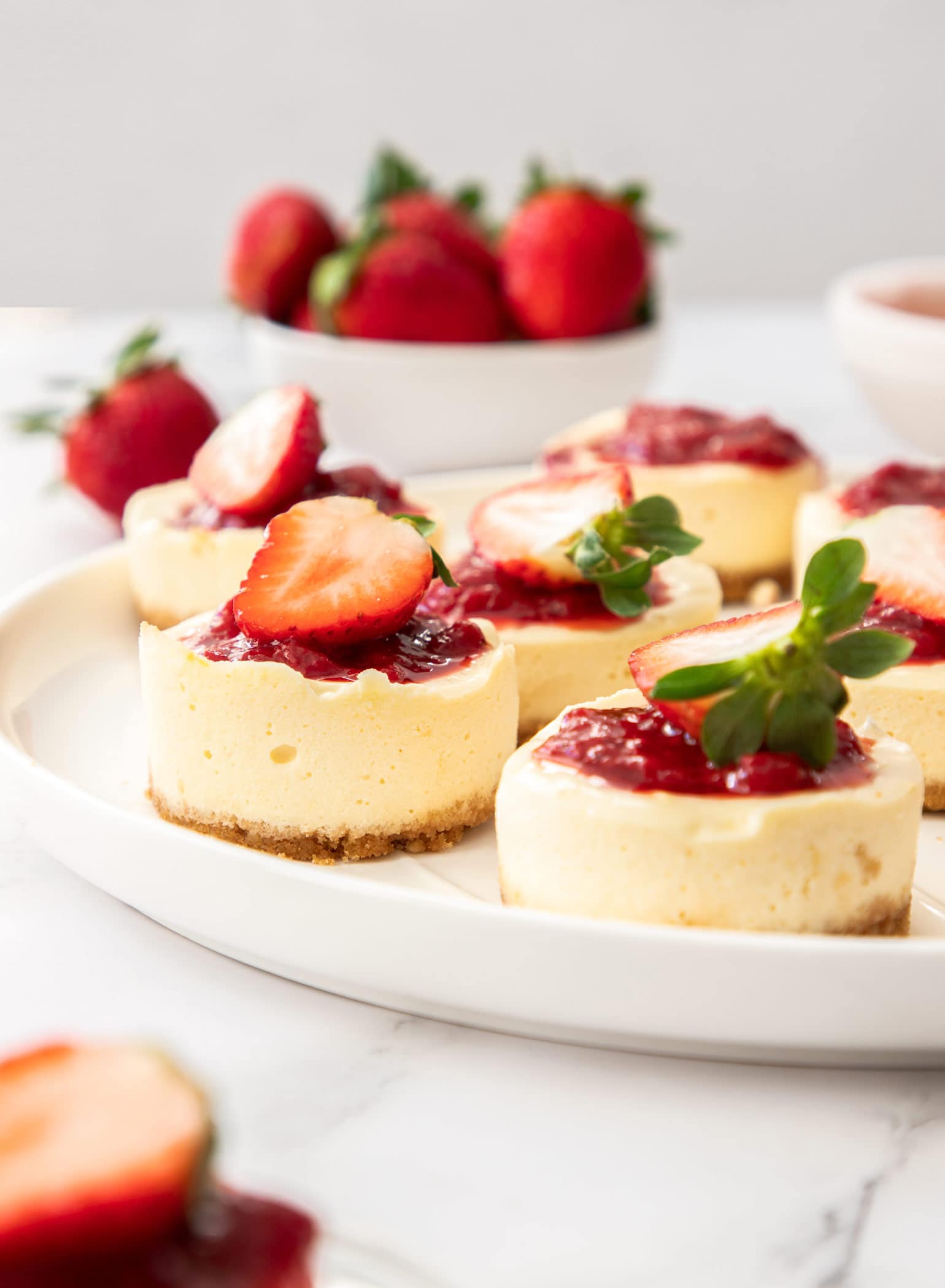 A large white plate with a batch of mini strawberry cheesecakes on it