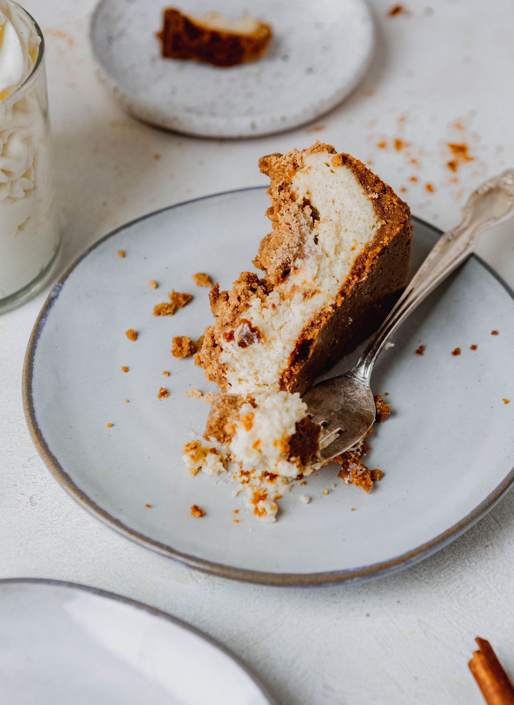 A serving of biscoff snickerdoodle cheese cake on a white dessert plate with a fork. The cheesecake is light and creamy in a crumb crust with cinnamon sugar snickerdoodle topping.