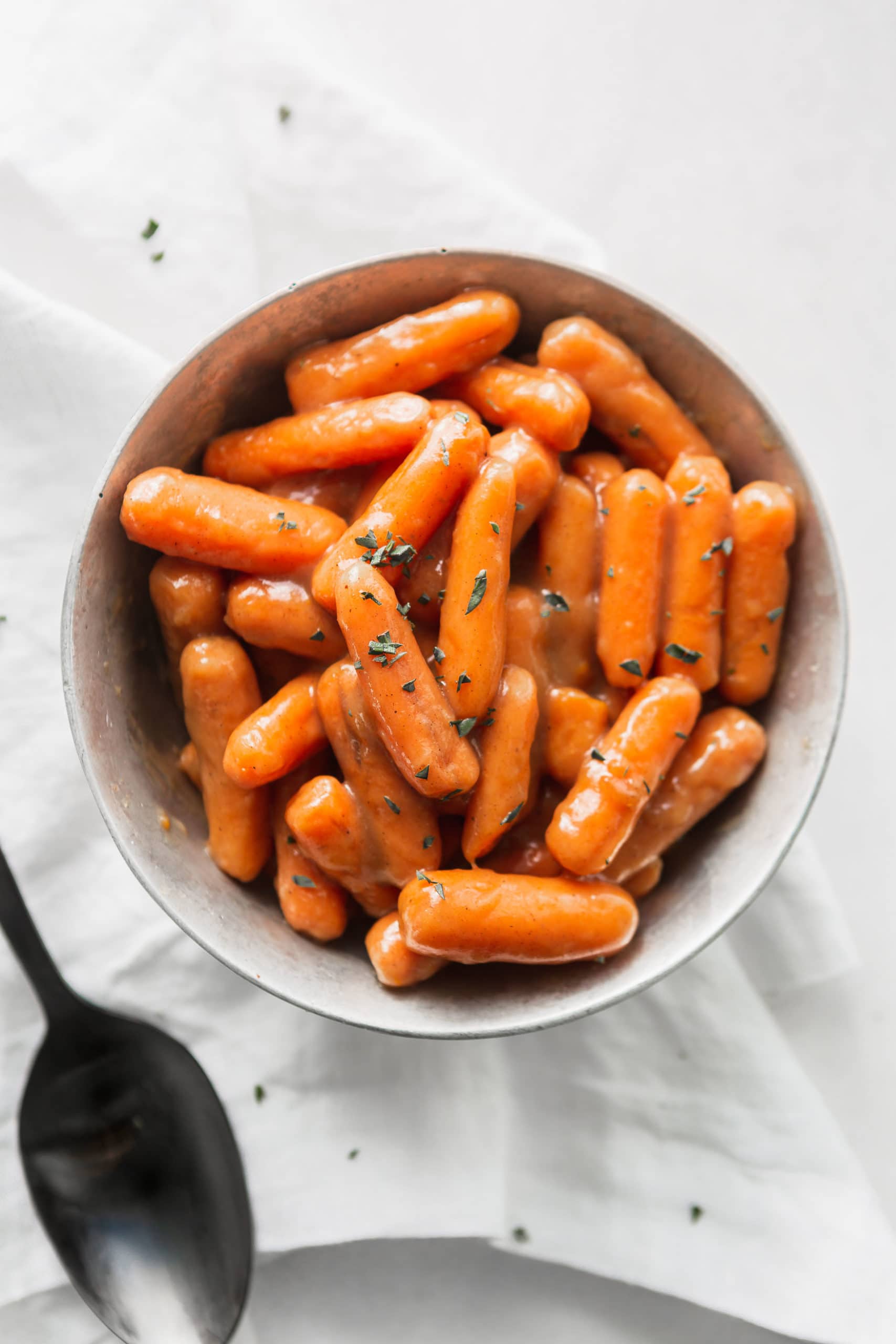 A bowl of orange glazed baby carrots. A serving spoon is next to the bowl.
