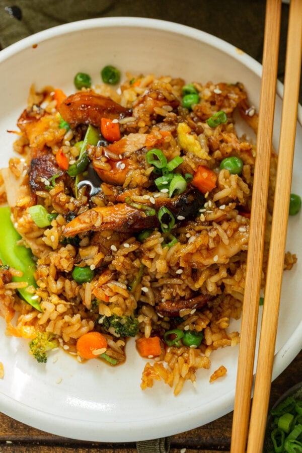 a photo of a dinner plate full of a teriyaki chicken casserole including fried rice, large chunks of chicken and assorted vegetables with chopsticks sitting on the side.