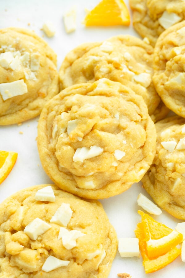 a photo of a golden baked orange creamsicle cookie loaded with white chocolate chunks and surrounded by other cookies.