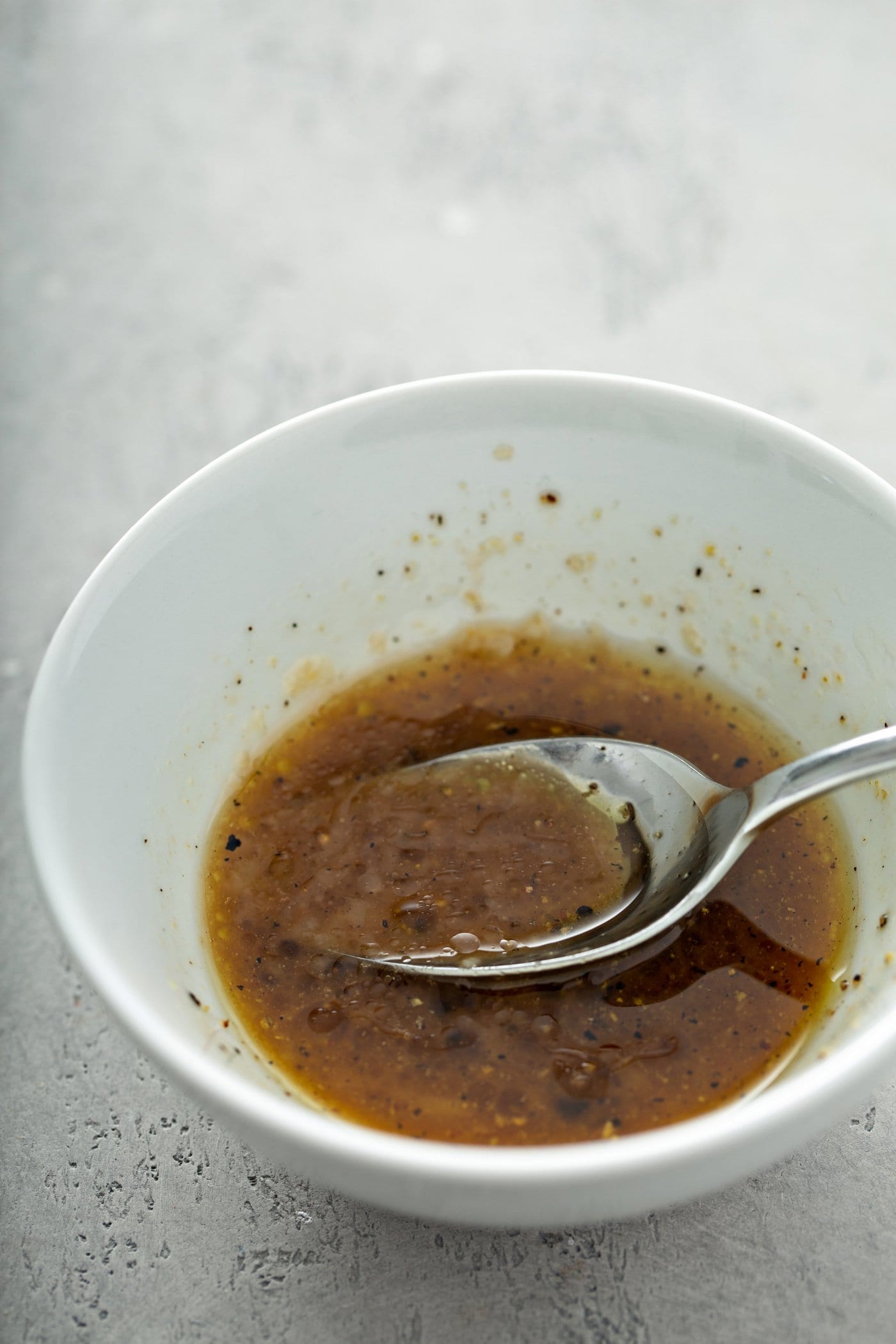 A white bowl containing balsamic glaze. There is a spoon in the bowl.