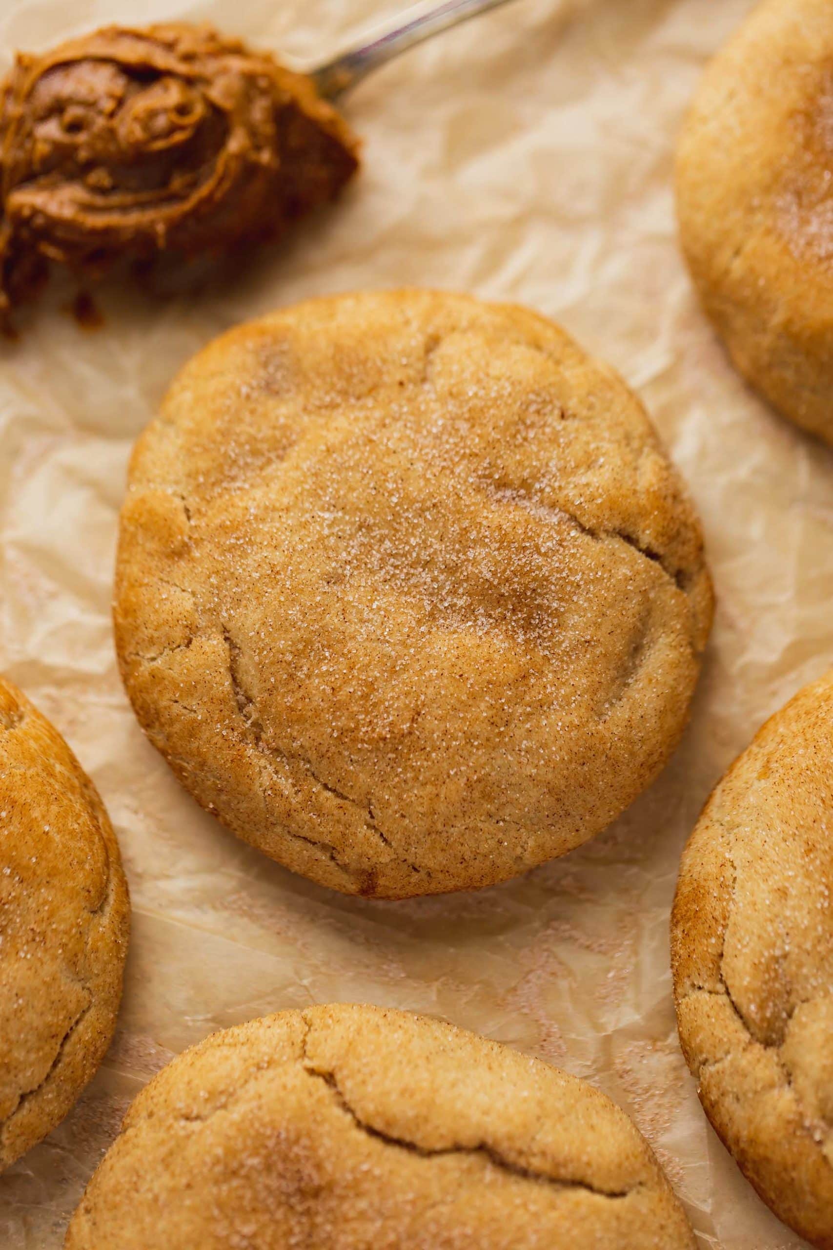 A baked biscoff stuffed snickerdoodle sprinkled with cinnamon sugar. There are other snickerdoodles around the cookie.
