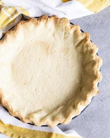 A par-bake pie crust on a gray surface next to a tea towel