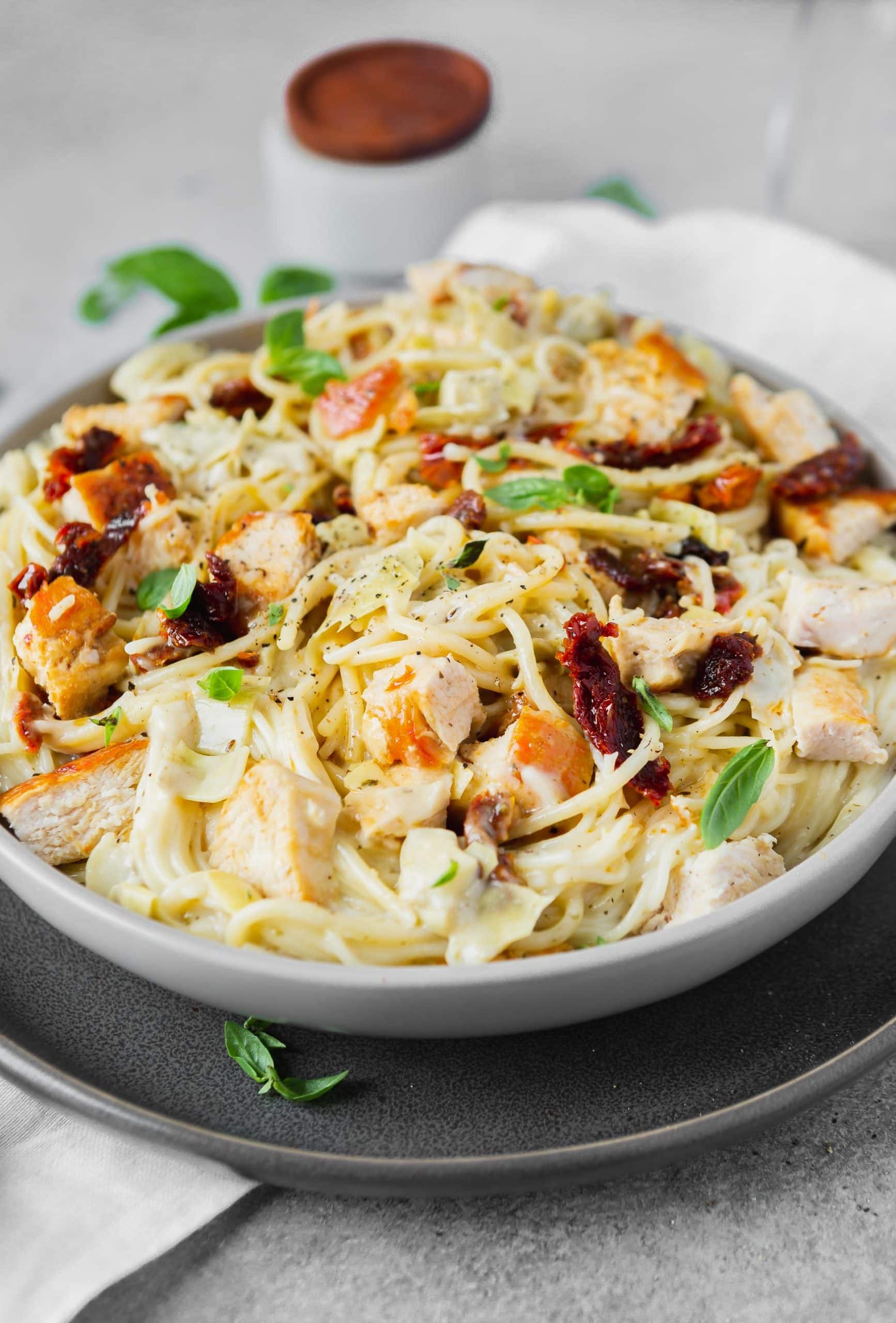a photo of creamy chicken artichoke pasta in a large bowl topped with large chunks of golden chicken breasts.