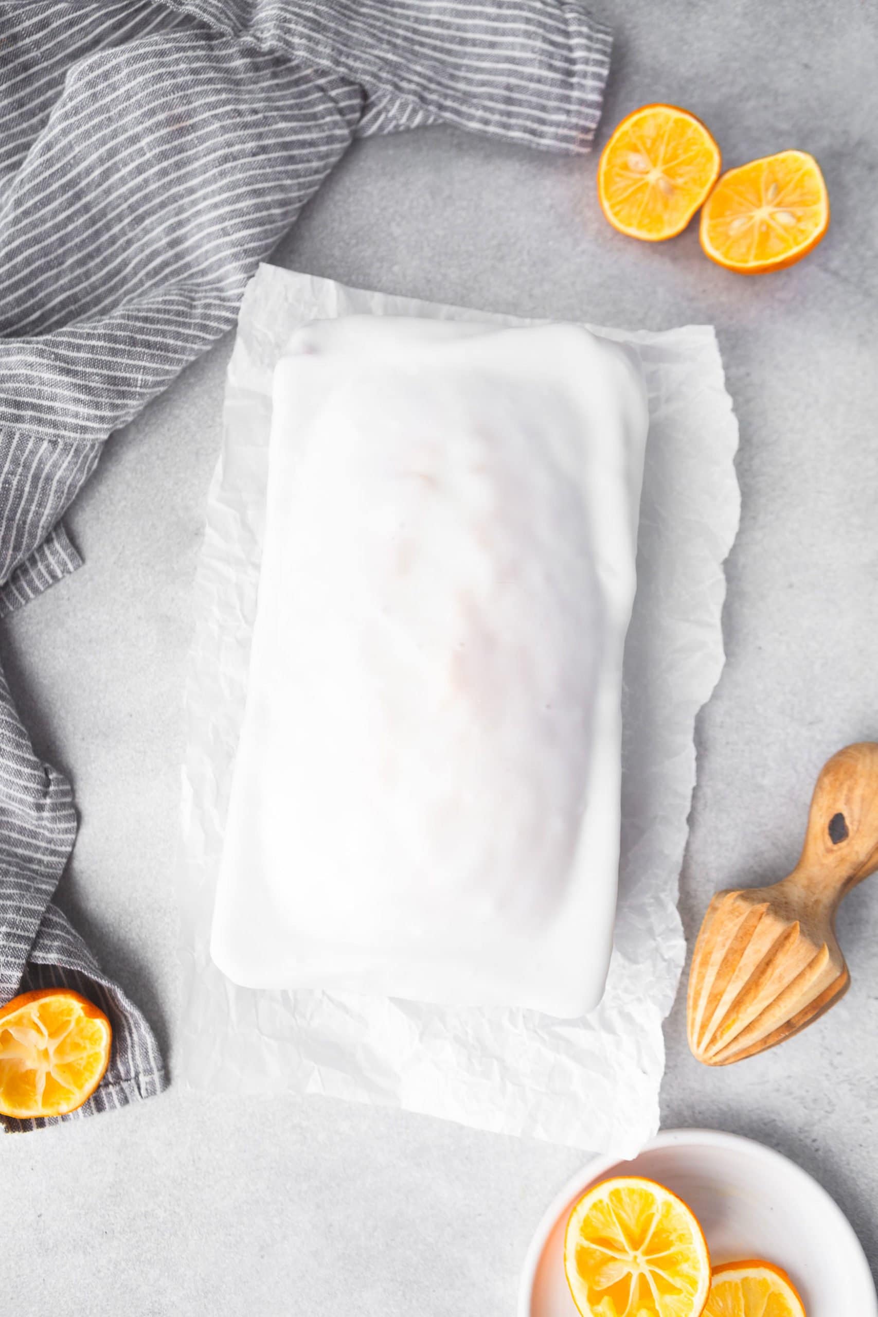a photo of a whole iced lemon loaf cake taken from above of cake. It is sitting on a torn piece of parchment with a wooden lemon reamer sitting next to it.