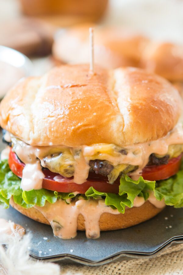a melty cheese burger with lettuce and tomatoes with burger sauce dripping down the sides a melty cheese burger with lettuce and tomatoes with burger sauce dripping down the sides