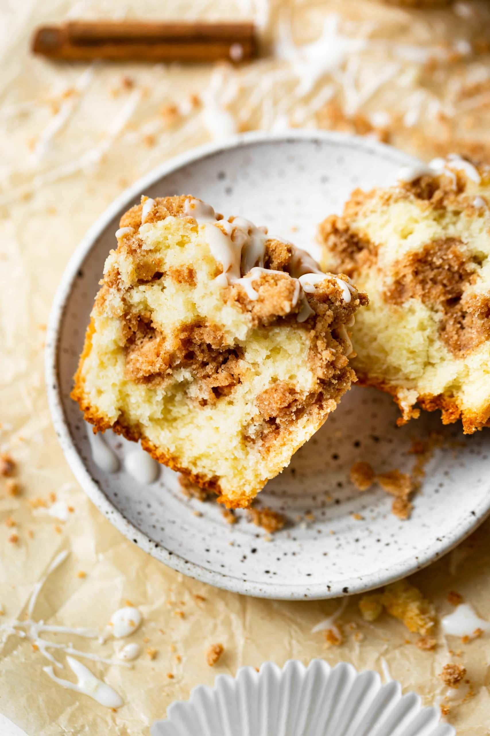 A photo of a coffee cake muffin that has been broken in half so you can see the inside of the muffin. There is streusel on top and in the middle of the baked muffin. A photo of a coffee cake muffin that has been broken in half so you can see the inside of the muffin. There is streusel on top and in the middle of the baked muffin.