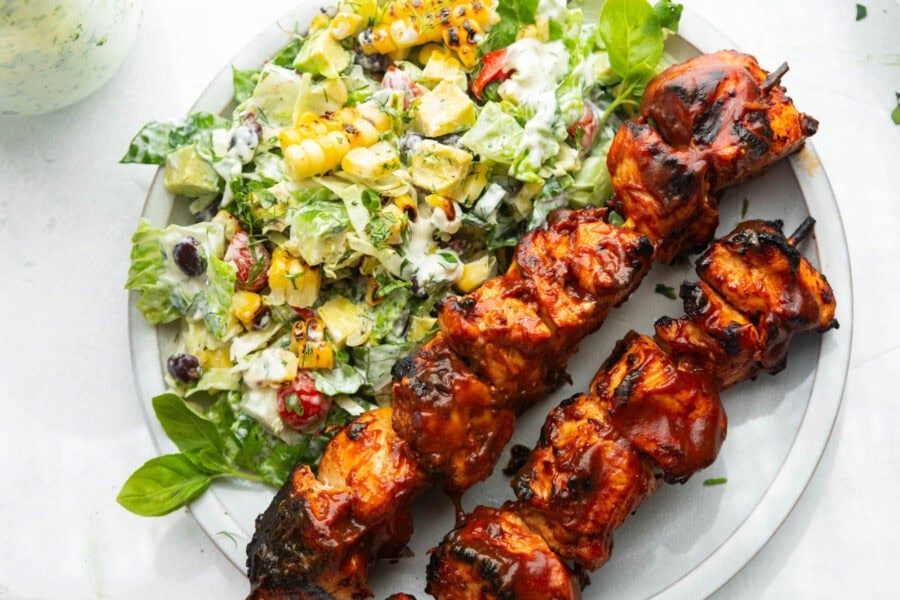 two saucy bbq chicken kabobs with creamy ranch salad on the side on a white dinner plate two saucy bbq chicken kabobs with creamy ranch salad on the side on a white dinner plate