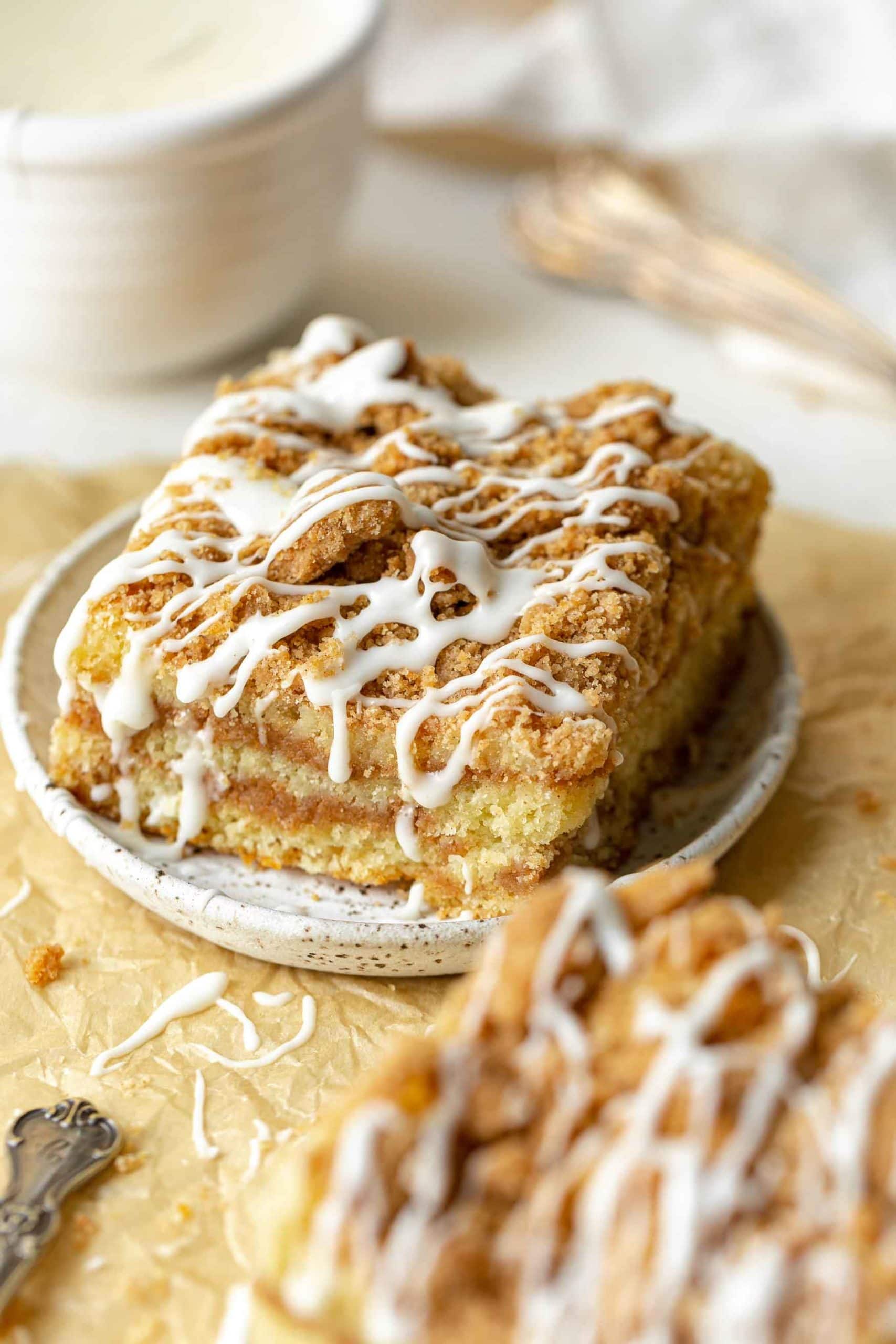 a photo of a piece of coffee cake topped with icing drizzles on a small saucer with another piece in the foreground. a photo of a piece of coffee cake topped with icing drizzles on a small saucer with another piece in the foreground.