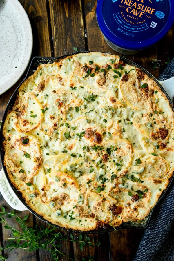 a photo of a large skillet full of creamy cheesy potatoes with a container of blue cheese sitting next to it a photo of a large skillet full of creamy cheesy potatoes with a container of blue cheese sitting next to it