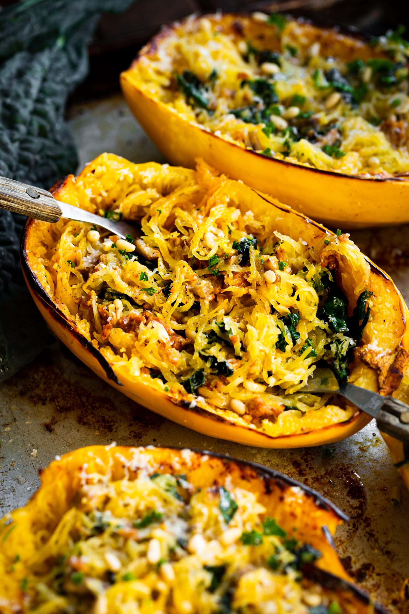 a photo of a spaghetti squash that has been halved and roasted facing up and filled with spaghetti squash mixed with kale, sausage, and topped with pine nuts and fresh parsley. a photo of a spaghetti squash that has been halved and roasted facing up and filled with spaghetti squash mixed with kale, sausage, and topped with pine nuts and fresh parsley.
