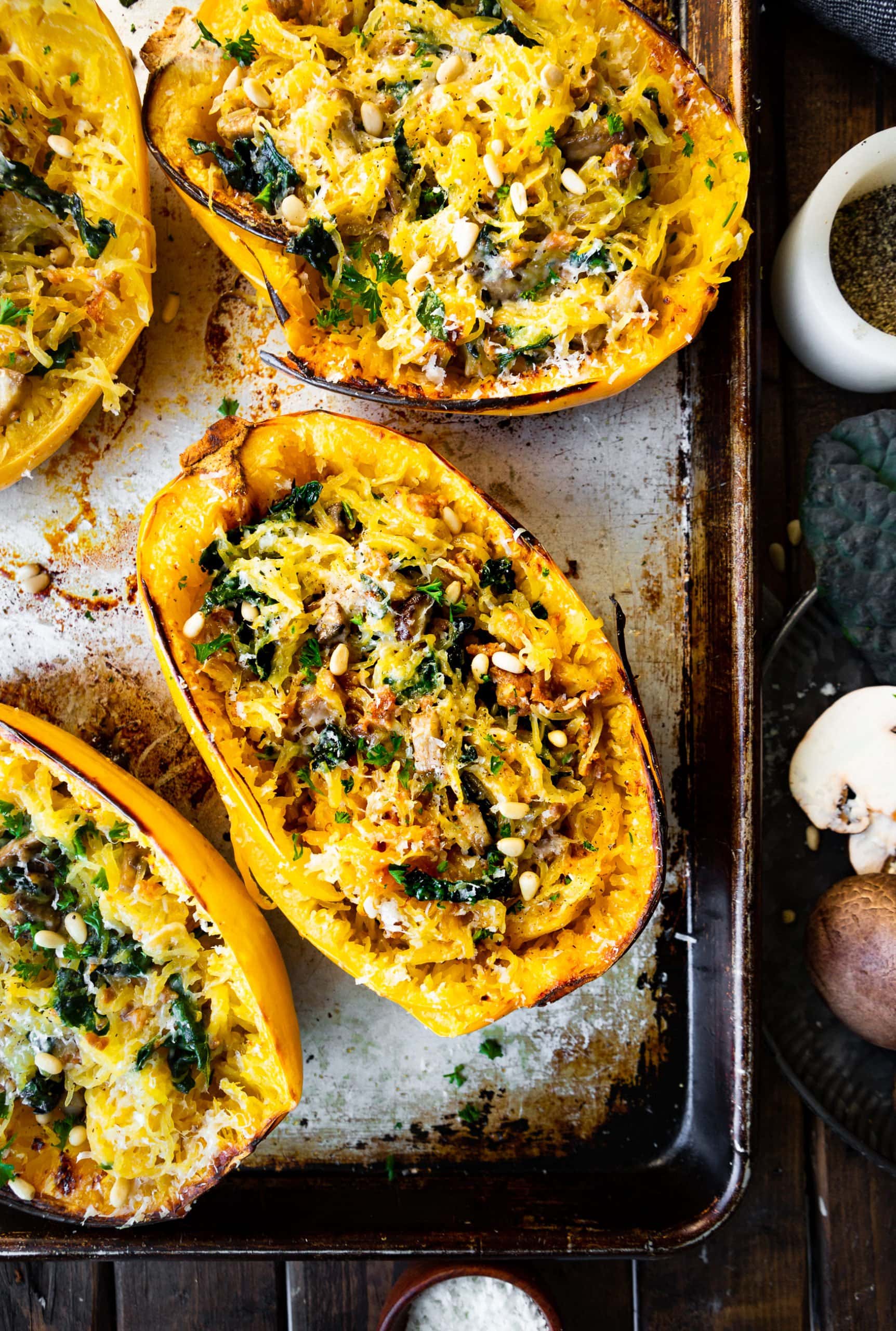 a photo of several halved brown butter squashes that have been roasted and stuffed with chopped kale, baby bella mushrooms, pine nuts and parmesan cheese. a photo of several halved brown butter squashes that have been roasted and stuffed with chopped kale, baby bella mushrooms, pine nuts and parmesan cheese.
