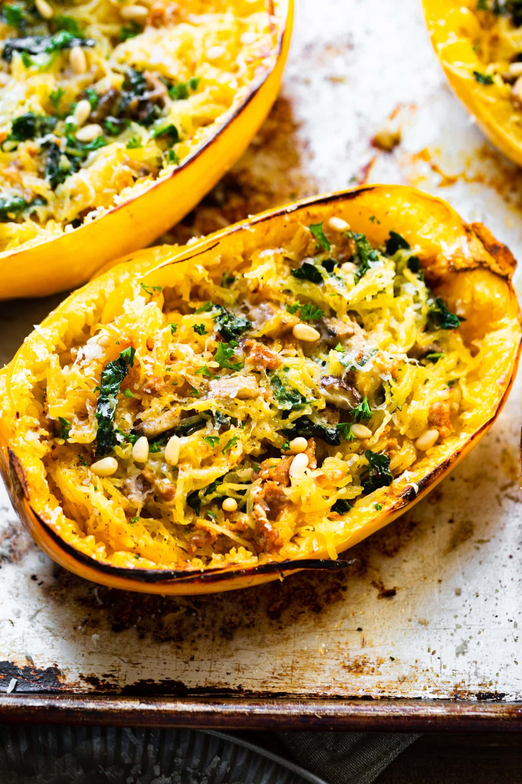 a photo of half of a spaghetti squash that has been roasted facing up and full of shredded spaghetti squash, chopped kale, pine nuts and garlic. a photo of half of a spaghetti squash that has been roasted facing up and full of shredded spaghetti squash, chopped kale, pine nuts and garlic.
