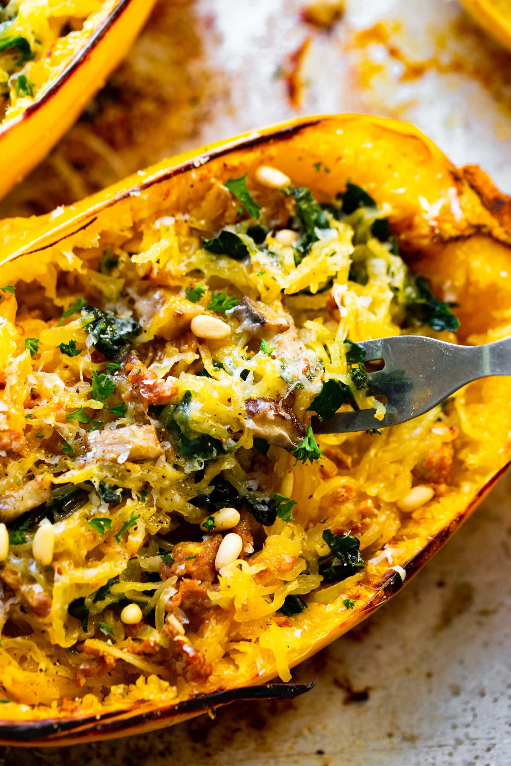 a photo of a fork digging into a halved spaghetti squash stuffed with cooked spaghetti squash, chopped kale, pine nuts, sausage and fresh parsley. a photo of a fork digging into a halved spaghetti squash stuffed with cooked spaghetti squash, chopped kale, pine nuts, sausage and fresh parsley.