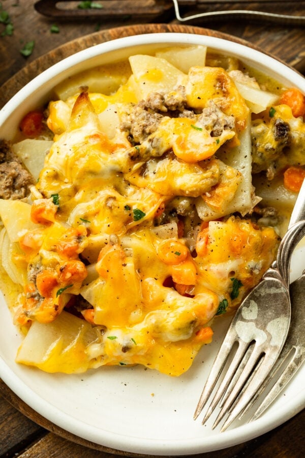 a photo of a dinner plate with a serving of cheesy ground beef and potato casserole on with two forks sitting next to it a photo of a dinner plate with a serving of cheesy ground beef and potato casserole on with two forks sitting next to it