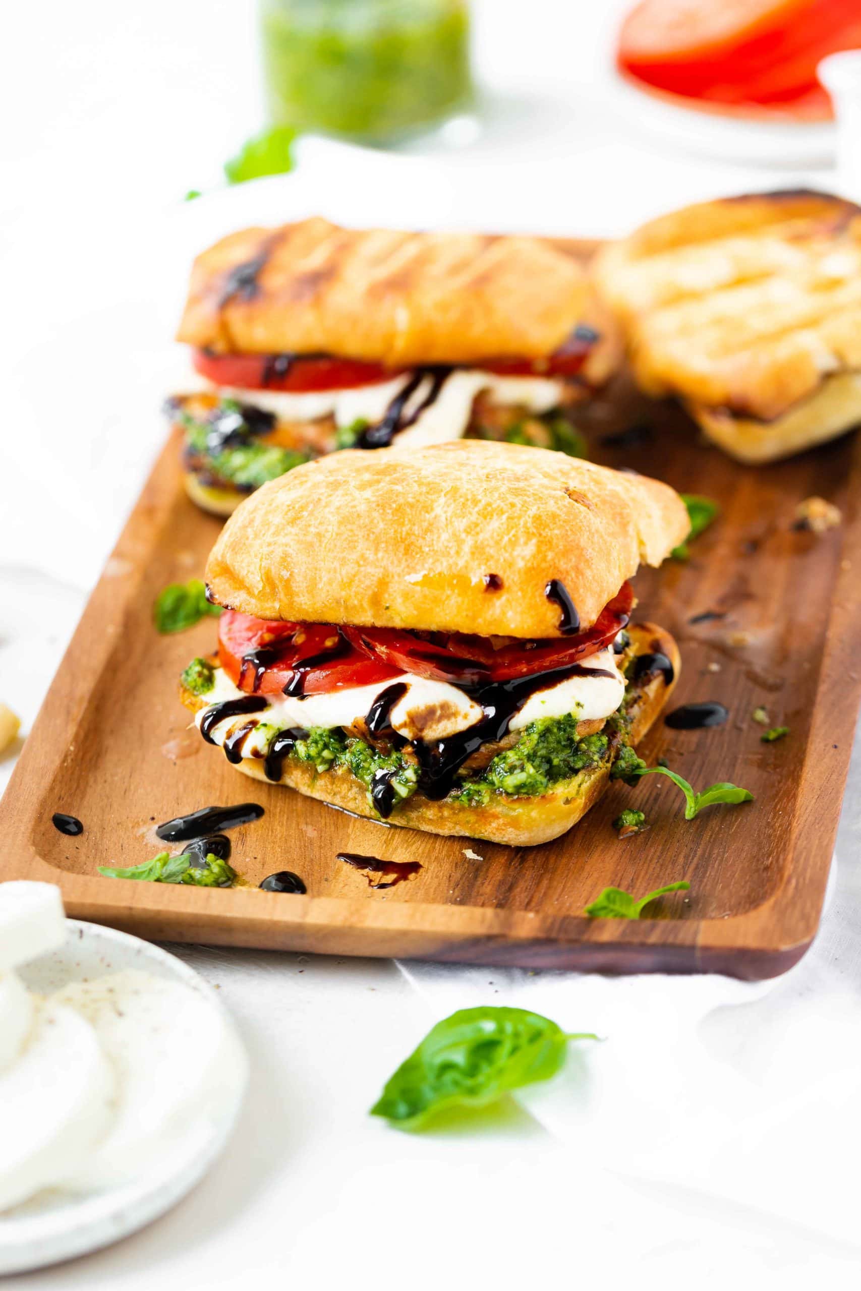 a photo of three chicken caprese sandwiches sitting on a wooden rectangular serving tray. a photo of three chicken caprese sandwiches sitting on a wooden rectangular serving tray.
