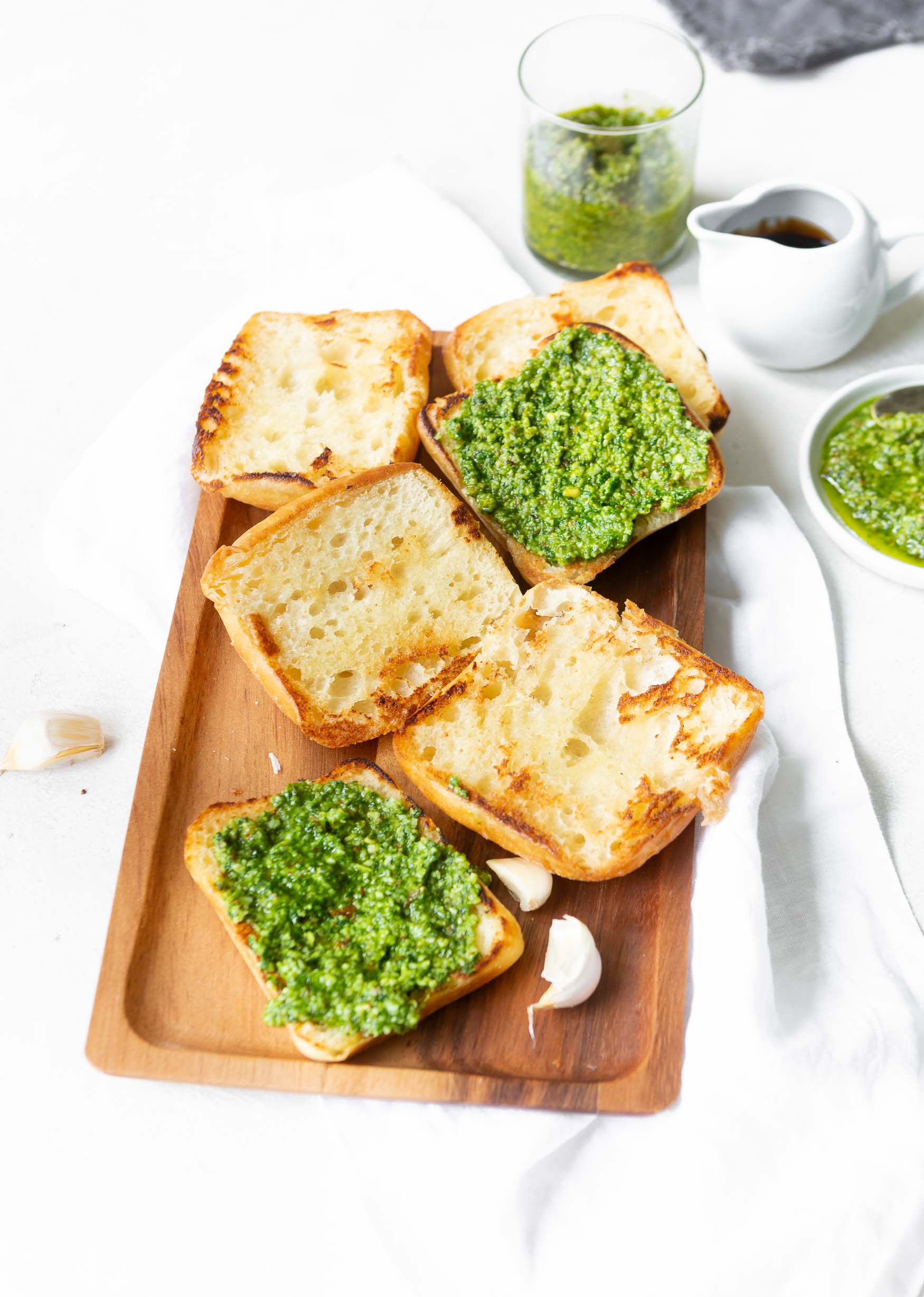 a photo of 3 ciabatta rolls sliced in half and toasted sitting face up on a wooden serving tray and 2 of the 6 slices have pesto spread on them. a photo of 3 ciabatta rolls sliced in half and toasted sitting face up on a wooden serving tray and 2 of the 6 slices have pesto spread on them.