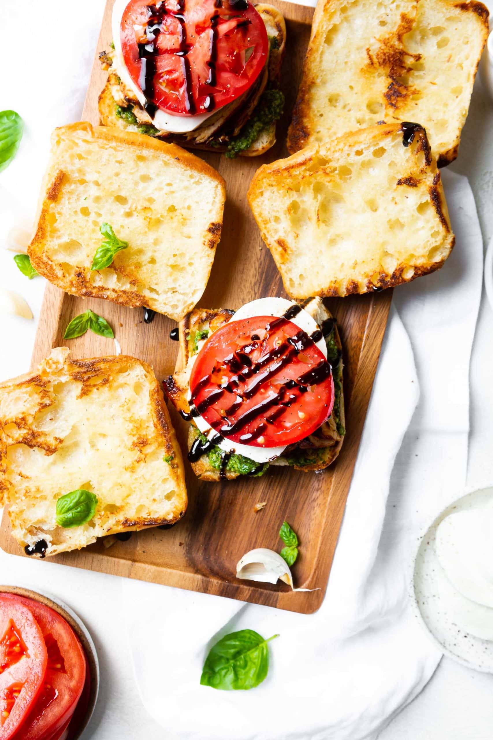 a photo of a ciabatta bun topped with pesto, fresh mozzarella, a tomato slice and a balsamic glaze with the top bun of the sandwich sitting next to it. a photo of a ciabatta bun topped with pesto, fresh mozzarella, a tomato slice and a balsamic glaze with the top bun of the sandwich sitting next to it.