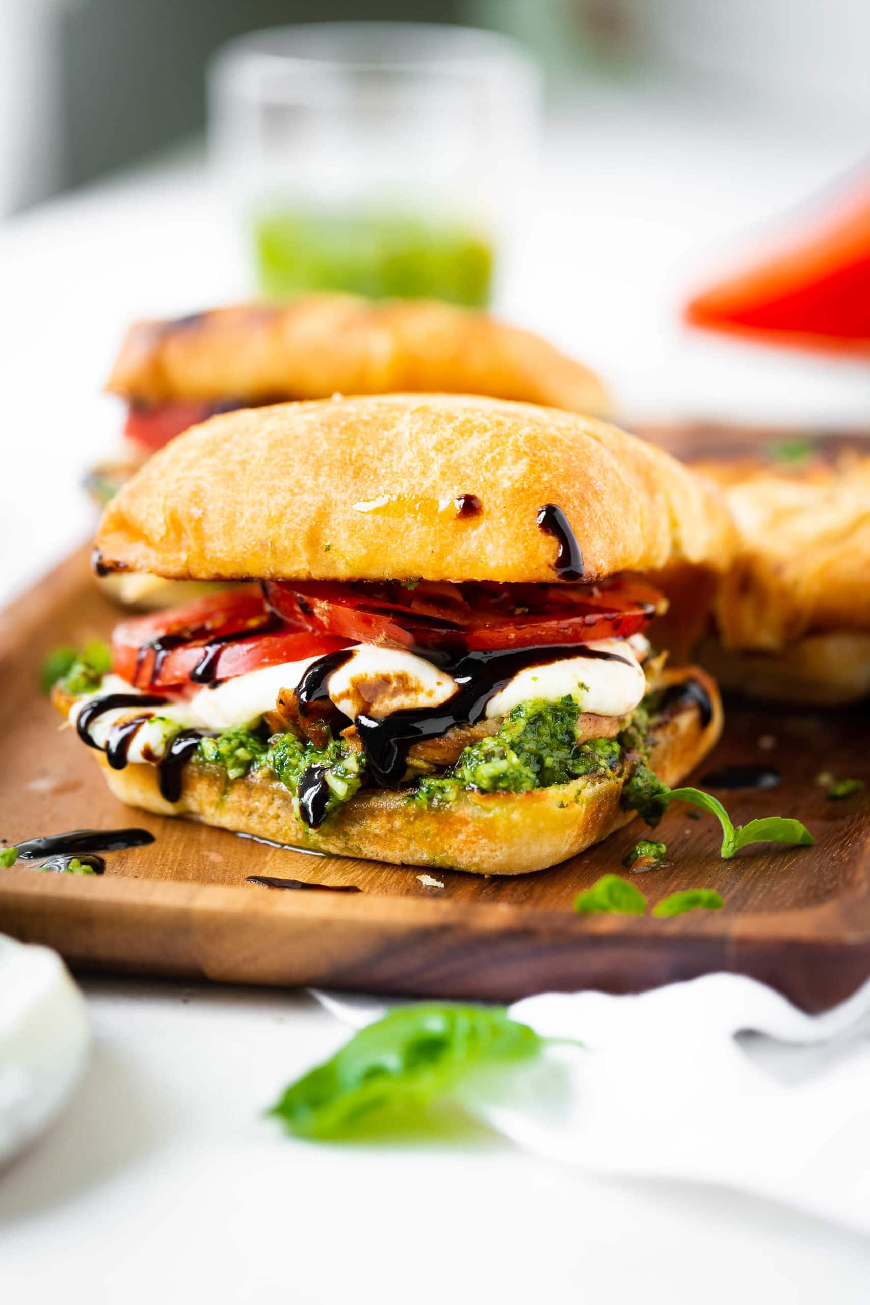 a photo of a chicken caprese sandwich completely assembled sitting on a wooden serving tray. The sandwich has pesto, fresh mozzarella, tomato, chicken, and balsamic glaze all on a toasted ciabatta bun. a photo of a chicken caprese sandwich completely assembled sitting on a wooden serving tray. The sandwich has pesto, fresh mozzarella, tomato, chicken, and balsamic glaze all on a toasted ciabatta bun.