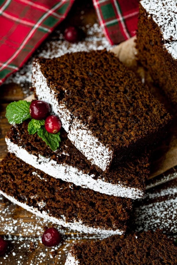 a photo of several slices of moist gingerbread loaf laying on each other topped with whole cranberries and greenery a photo of several slices of moist gingerbread loaf laying on each other topped with whole cranberries and greenery