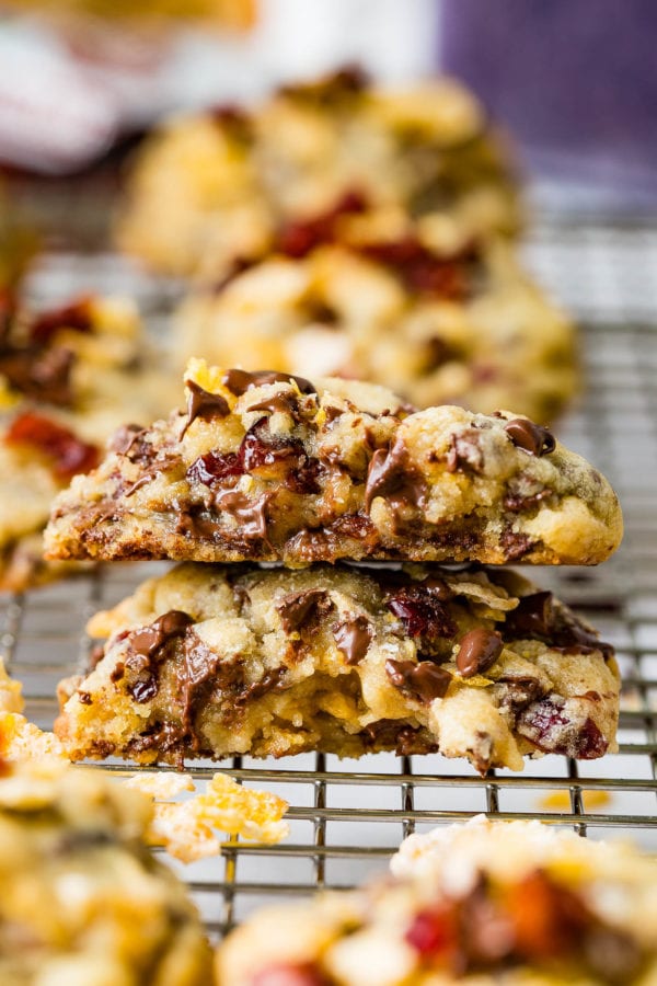 A craisin frosted flake cookie that is broken in half and stacked on top of each other. Other cookies are in the background. A craisin frosted flake cookie that is broken in half and stacked on top of each other. Other cookies are in the background.