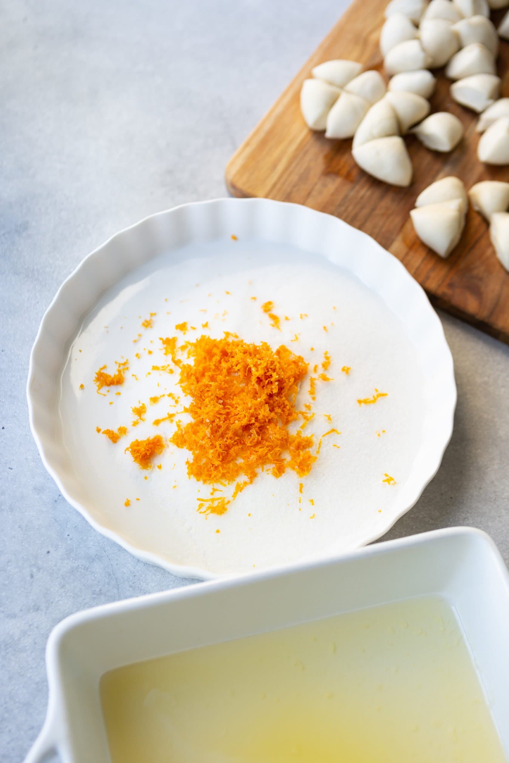 a white dish with sugar and orange zest, another with butter and finally cut up bread dough a white dish with sugar and orange zest, another with butter and finally cut up bread dough