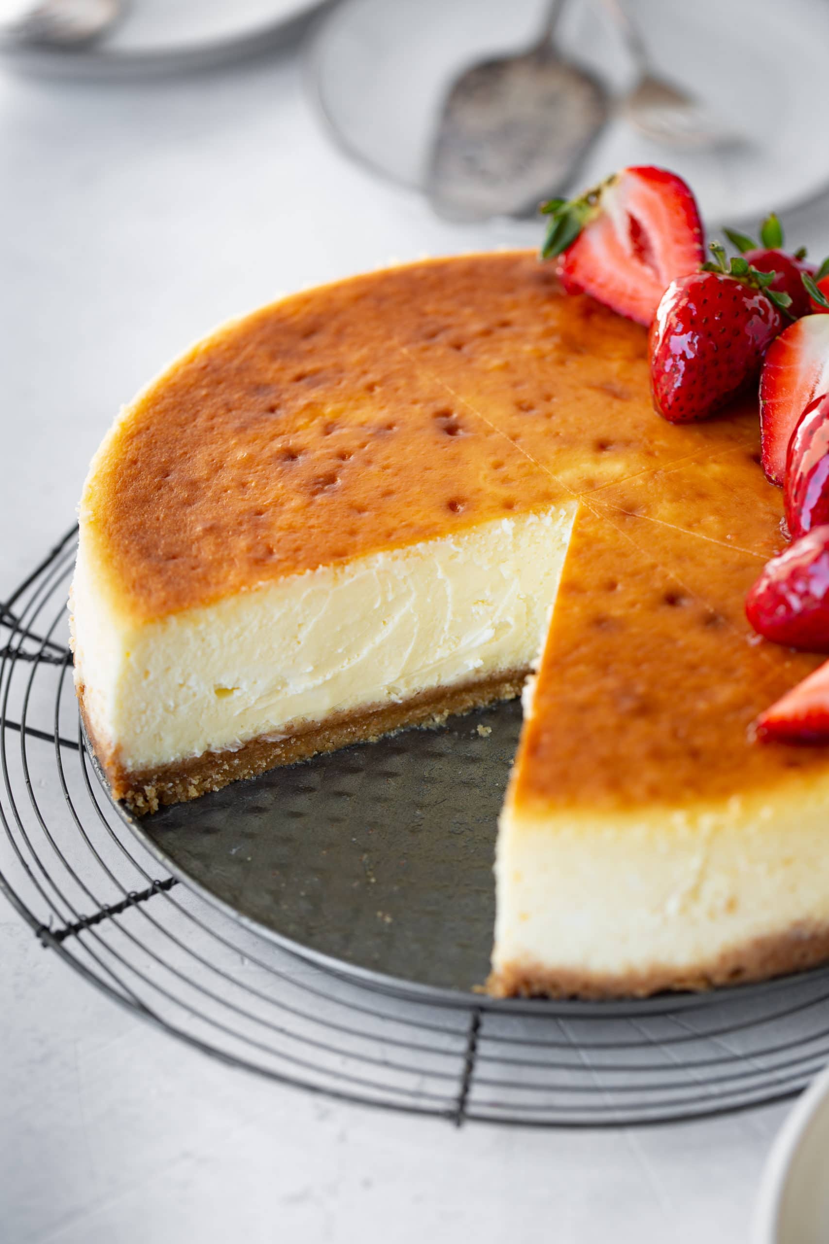 a photo of a whole cheesecake topped with glazed whole and halved strawberries with a couple of slices removed so you can see the perfect bake through the middle of the cheesecake. a photo of a whole cheesecake topped with glazed whole and halved strawberries with a couple of slices removed so you can see the perfect bake through the middle of the cheesecake.