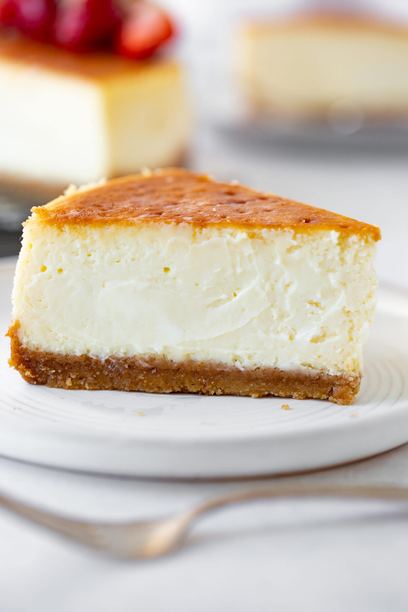 a photo of a large slice of classic cheesecake taken from the side so you can see the cross-section. It has a thick graham cracker crust and golden top. a photo of a large slice of classic cheesecake taken from the side so you can see the cross-section. It has a thick graham cracker crust and golden top.