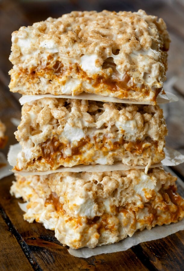 a photo of three dulce de leche stuffed gooey rice krispie treats stacked on top of each other with little pieces of parchment paper between them. a photo of three dulce de leche stuffed gooey rice krispie treats stacked on top of each other with little pieces of parchment paper between them.