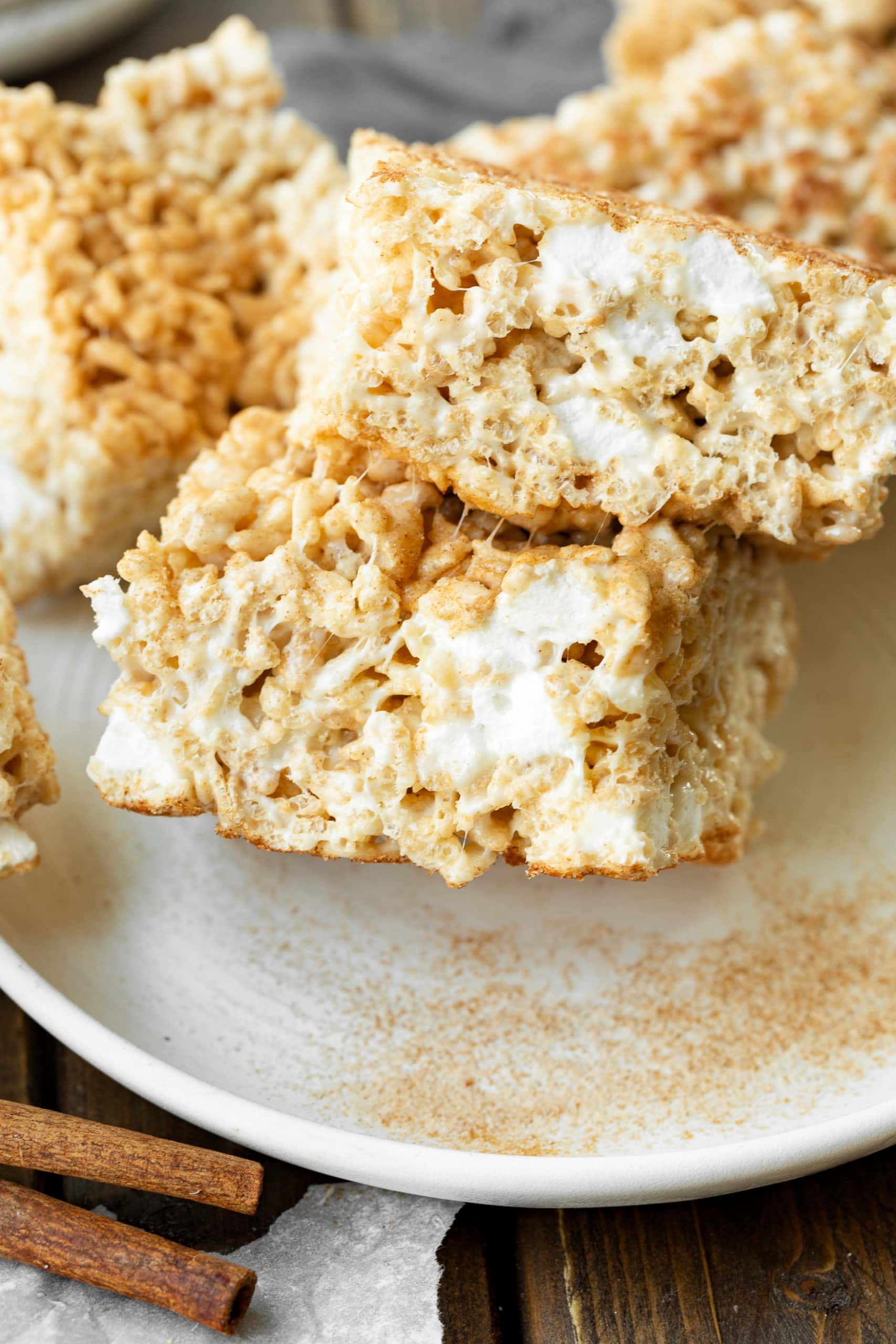 a photo of two thick square rice krispie treats stacked on top of each other so you can see the gooey cross-section of the bar dessert. a photo of two thick square rice krispie treats stacked on top of each other so you can see the gooey cross-section of the bar dessert.