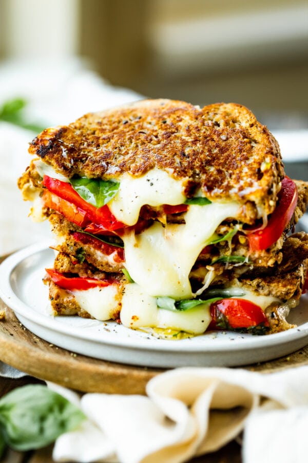 a photo of several halved grilled cheese sandwiches stacked on top of each other so you can see the cheese melting out of it and the layers of tomato and fresh basil. a photo of several halved grilled cheese sandwiches stacked on top of each other so you can see the cheese melting out of it and the layers of tomato and fresh basil.