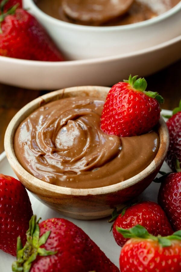 a photo of a small bowl filled with creamy chocolate yogurt dip with a whole strawberry dipped in it and strawberries scattered all around it a photo of a small bowl filled with creamy chocolate yogurt dip with a whole strawberry dipped in it and strawberries scattered all around it