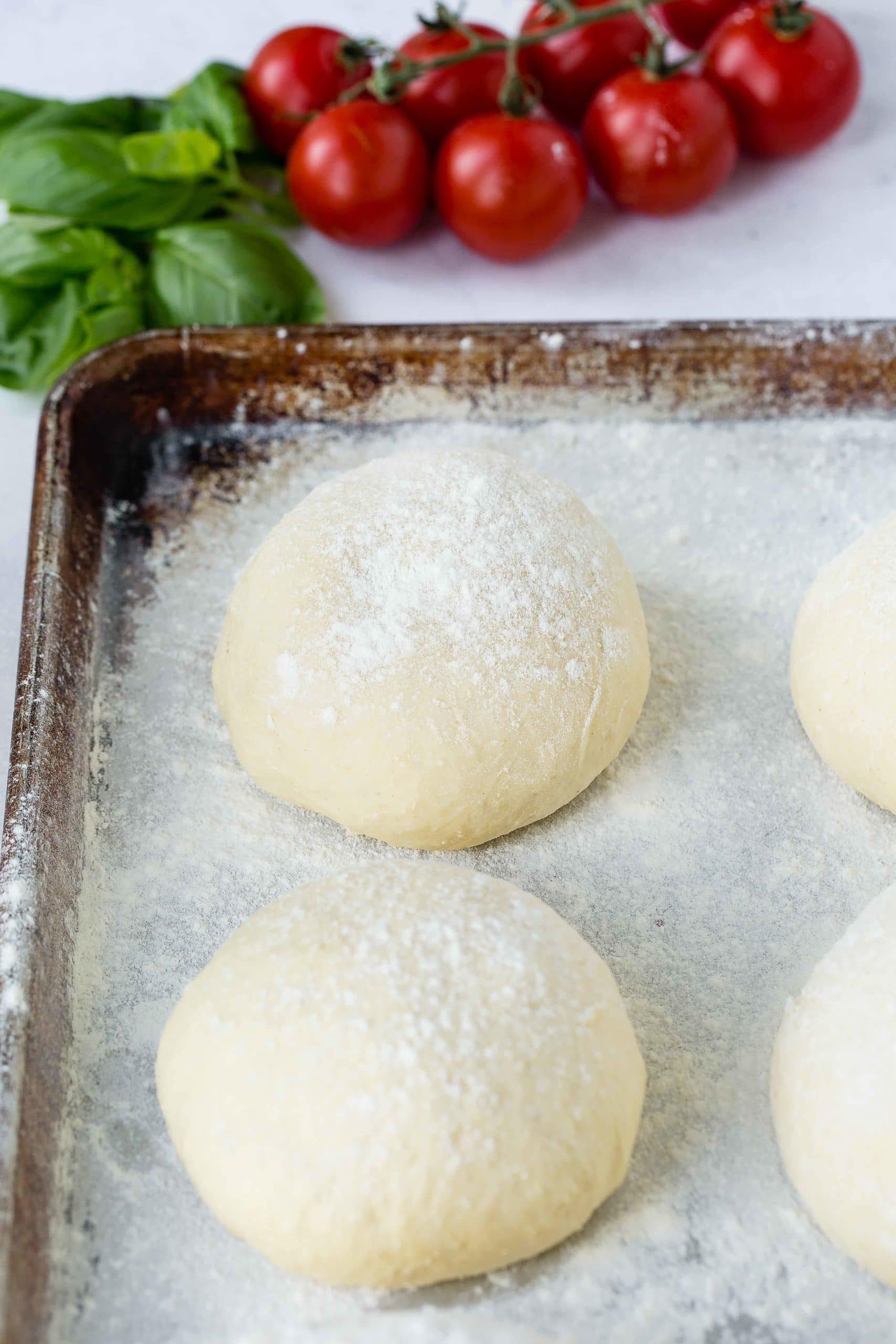 a photo of four round balls of pizza dough dusted with flour on top sitting on a baking sheet. a photo of four round balls of pizza dough dusted with flour on top sitting on a baking sheet.
