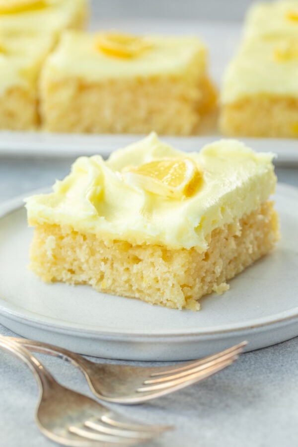 a photo of a square slice of moist lemon cake topped with lemon cream cheese frosting and a thin slice of fresh lemon on top a photo of a square slice of moist lemon cake topped with lemon cream cheese frosting and a thin slice of fresh lemon on top