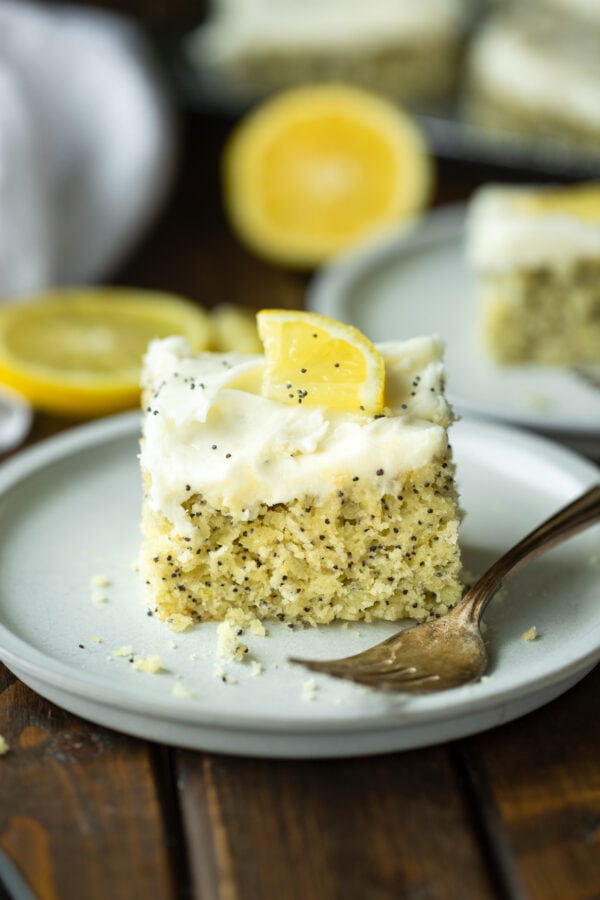 a photo of a piece of lemon poppy seed cake topped with a white cream cheese frosting and small lemon slice a photo of a piece of lemon poppy seed cake topped with a white cream cheese frosting and small lemon slice