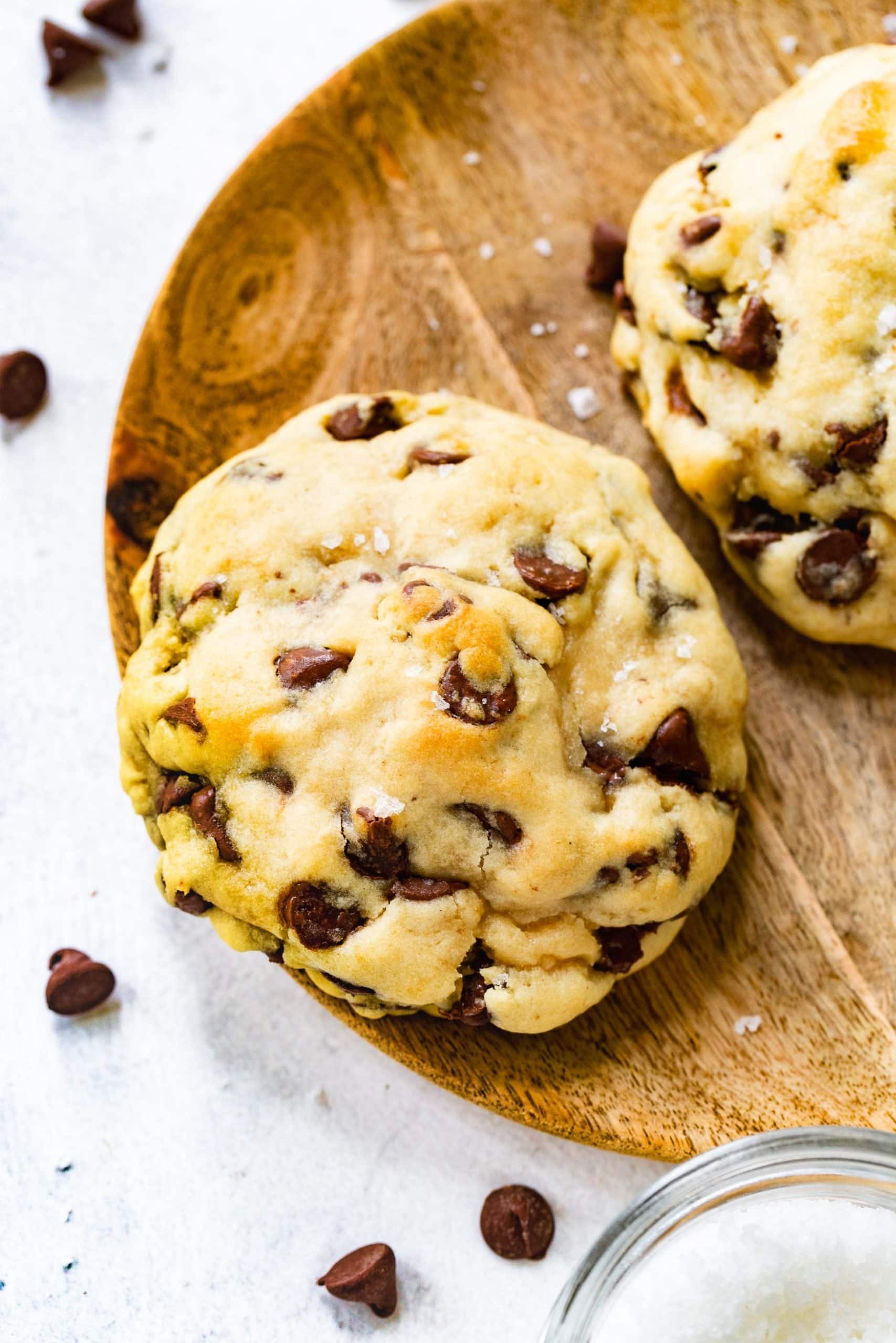 a thick chocolate chip cookie on a wooden plate with chocolate chips around it a thick chocolate chip cookie on a wooden plate with chocolate chips around it