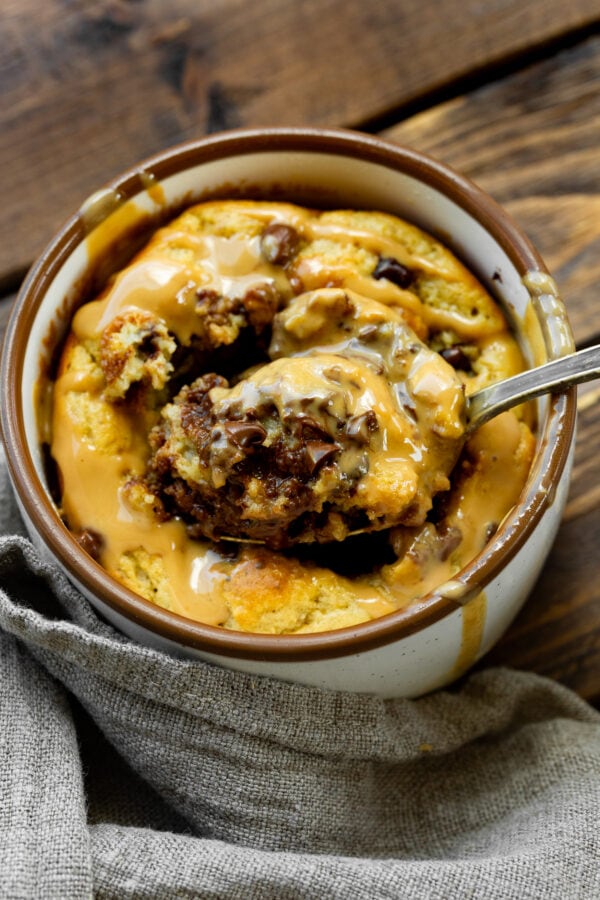 a photo of a mug full of baked oatmeal peanut butter and chocolate mug cake and someone is removing a spoonful of cake from the middle. a photo of a mug full of baked oatmeal peanut butter and chocolate mug cake and someone is removing a spoonful of cake from the middle.