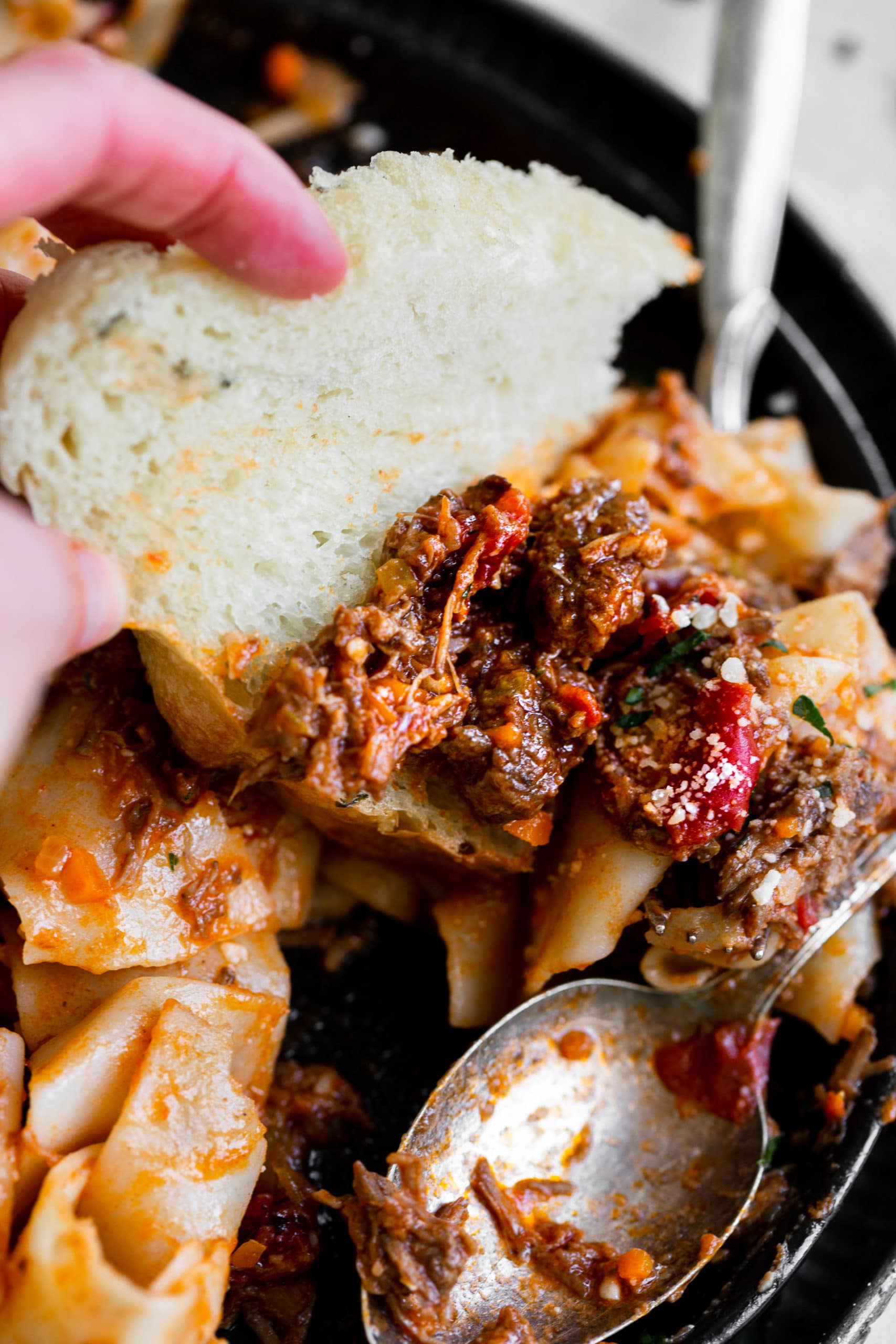 a photo of a someone scooping up some short rib ragu onto a piece of herbed peasant bread. a photo of a someone scooping up some short rib ragu onto a piece of herbed peasant bread.