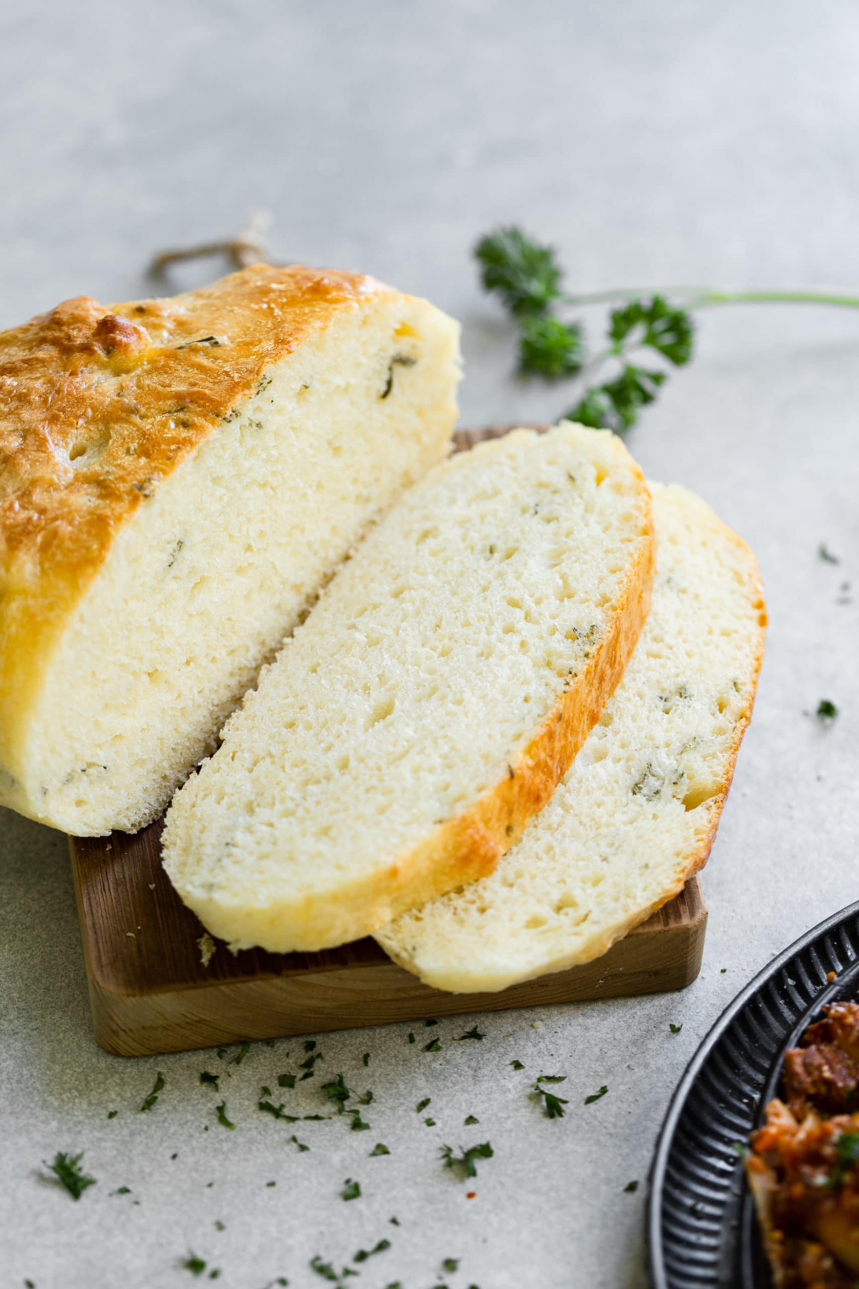 a photo of a golden baked loaf of herbed peasant bread that has been sliced into with a couple of slices sitting next to half of the loaf. a photo of a golden baked loaf of herbed peasant bread that has been sliced into with a couple of slices sitting next to half of the loaf.