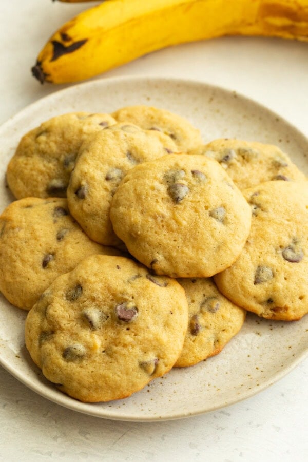 Soft chocolate chip cookies on white ceramic plate with banana in background. Soft chocolate chip cookies on white ceramic plate with banana in background.